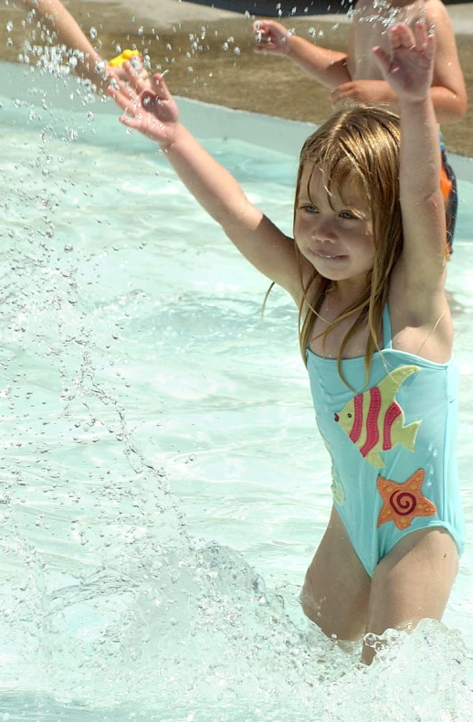 a young child in a swimming suit holds her hands above their head while another child watches