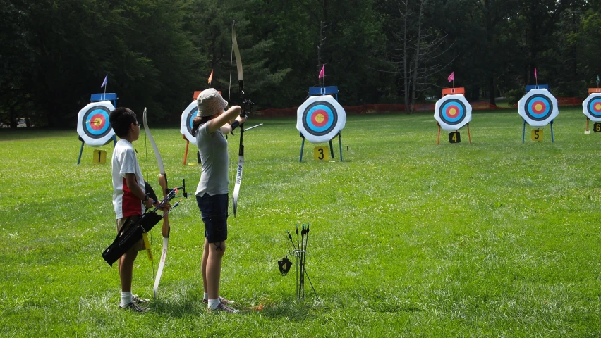 two people stand in front of several target bows and practice them at the park