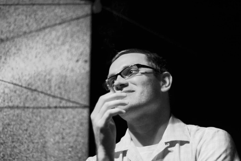 man wearing glasses sitting near wall, looking up at soing