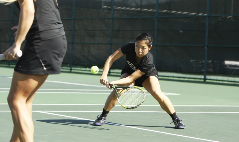 a woman in a black tennis outfit swings at a tennis ball with a racket on the court