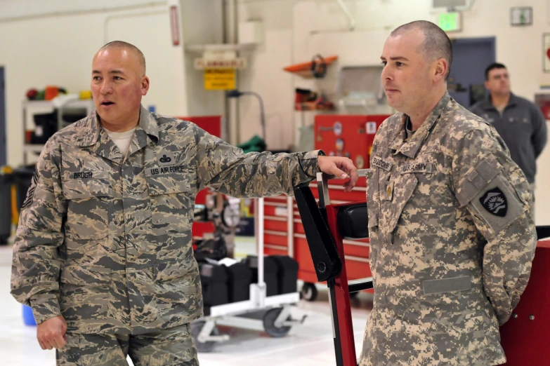 two soldiers stand talking in a building with other people