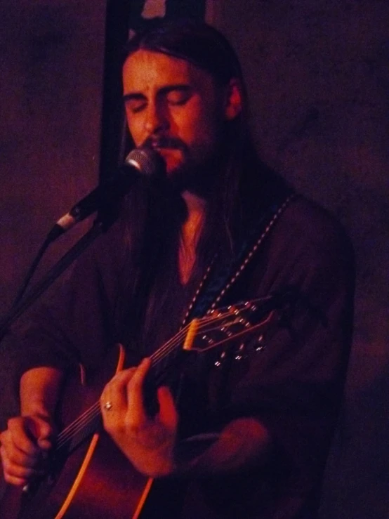 man with beard playing guitar and microphone in a dimly lit room