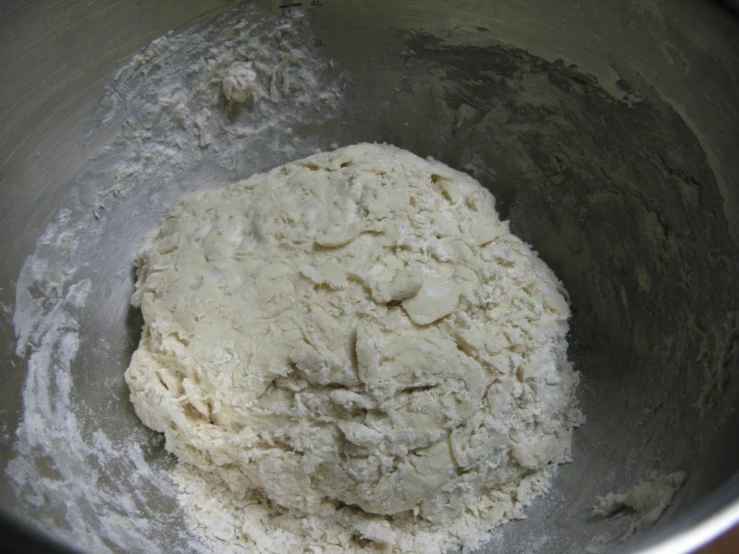 a silver mixing bowl filled with batter that is on top of flour