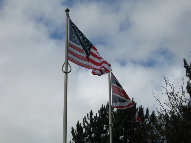 two american flags waving in the wind under a cloudy sky