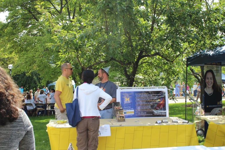 a group of people talking to each other outside in the shade