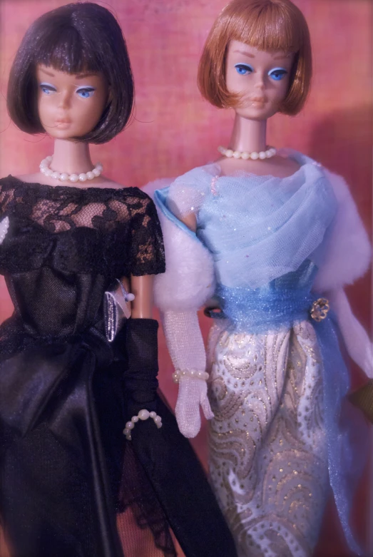 two dolls dressed in vintage clothing standing next to each other