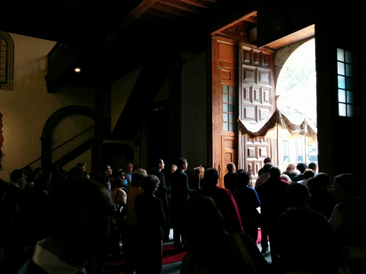 a crowd of people stand in line in front of a door at a church