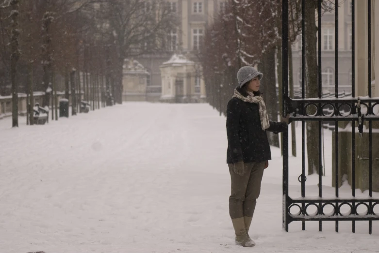 a person standing on a snowy road next to an iron gate