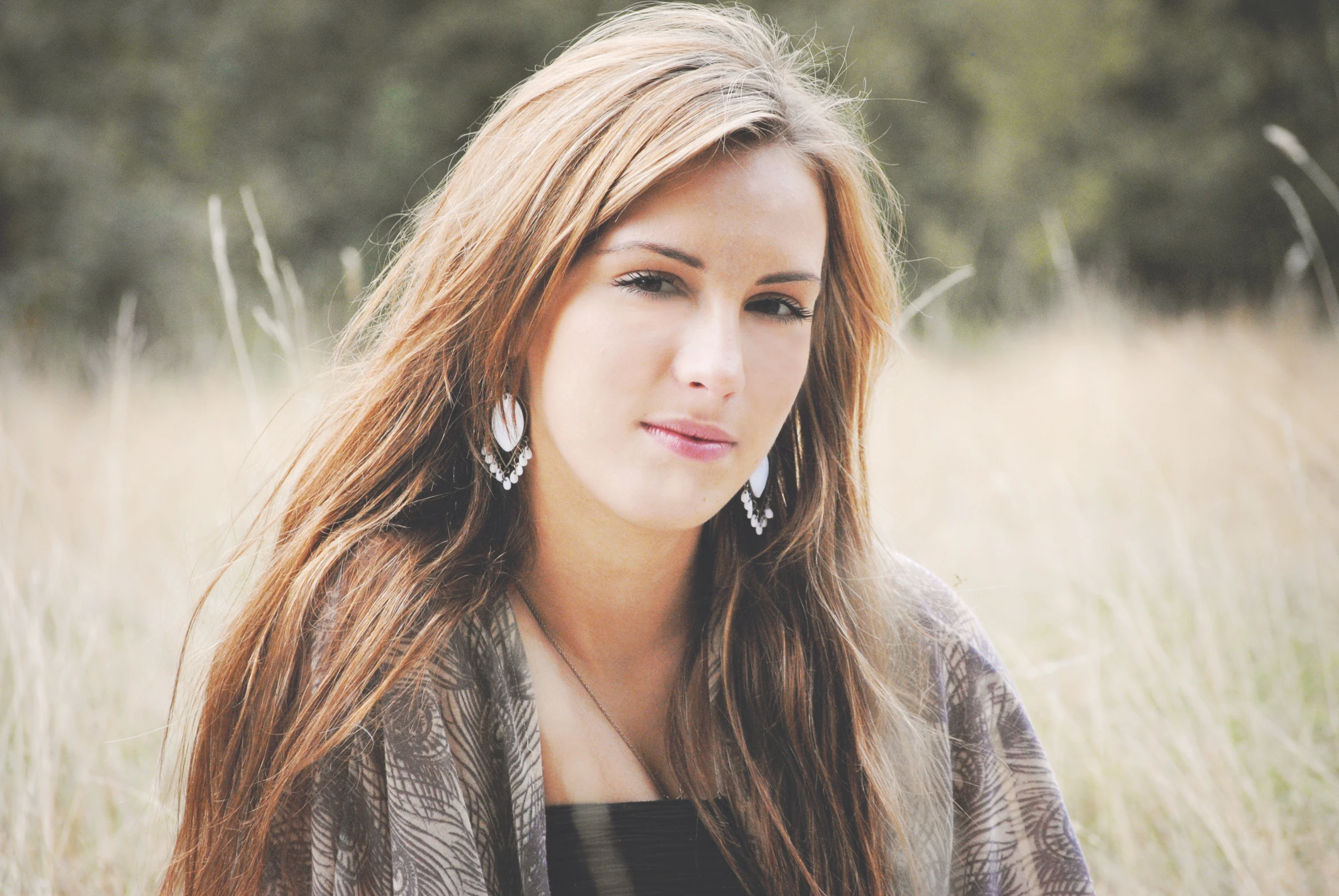 the woman is sitting in tall grass with her hair blowing