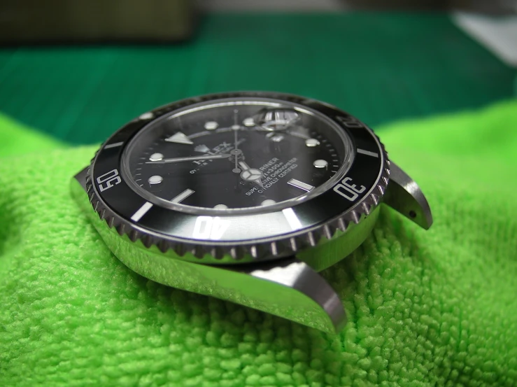 the black rolex watch is on a green blanket