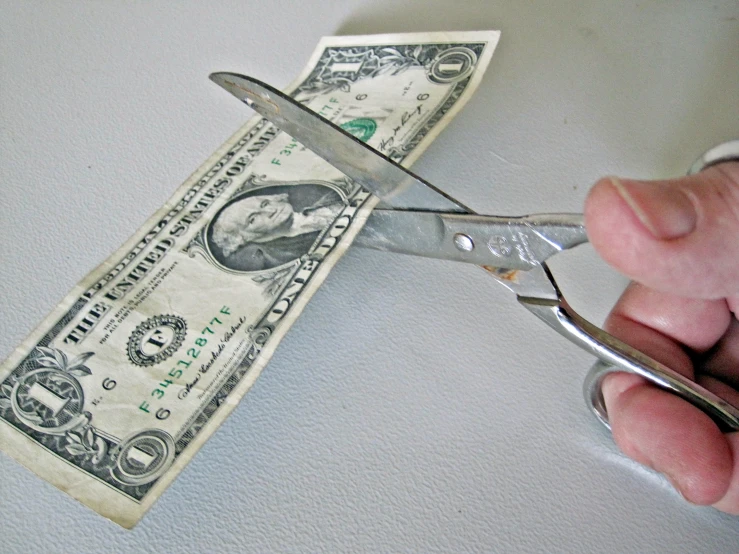 a hand with a pair of scissors  a one dollar bill