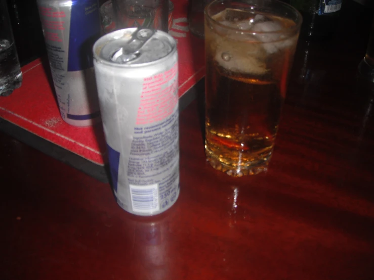 a drink in a glass sitting next to a can on a table