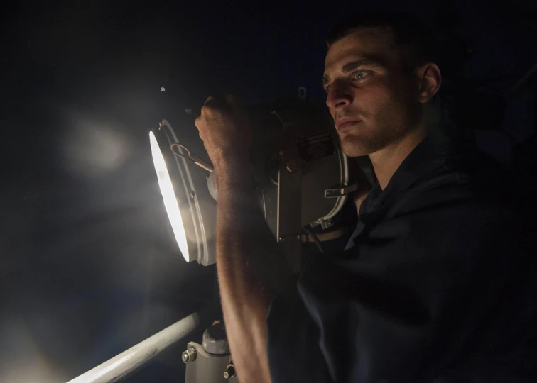 man sitting on balcony holding flashlight with dark background