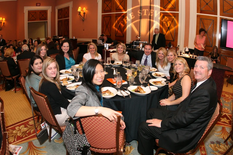 group of people sitting around dinner table with white plates on them