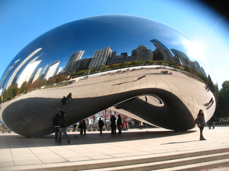 people walk by an enormous stainless sculpture that resembles the shape of a snake