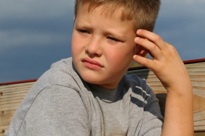 a boy wearing a gray sweatshirt holding his hands on his ear