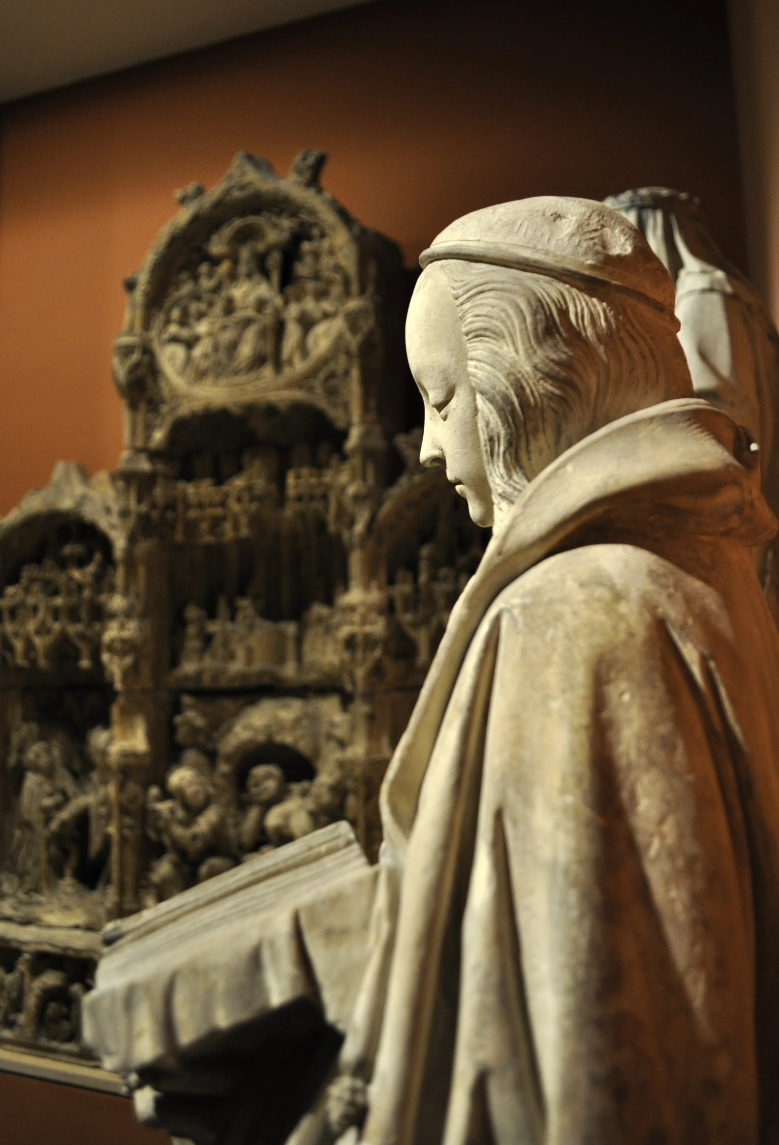 statue, depicting woman head and arms, sitting in front of an ornate piece