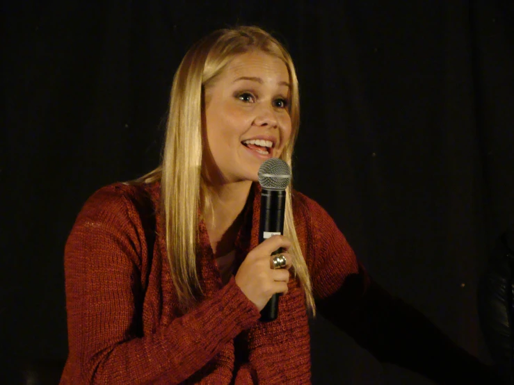 a woman with blonde hair wearing a red sweater holding a microphone