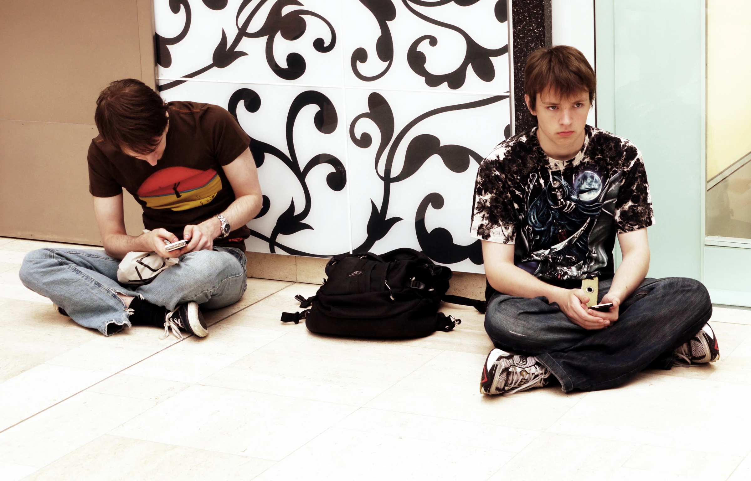 two men sitting on the ground while using their cellphones