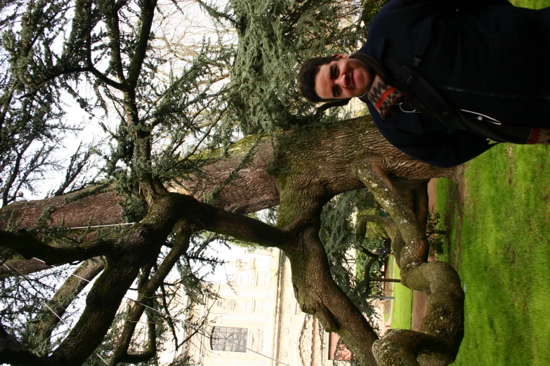 a man poses in front of a very large, old tree