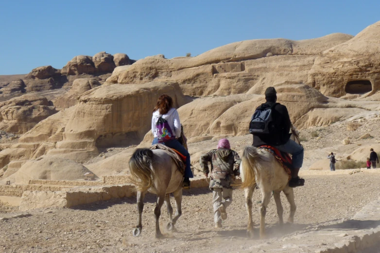 two people ride on horseback past some small rocks