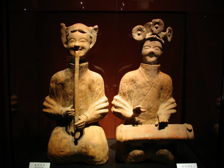 two old statues of man with big heads, and a woman with a bird