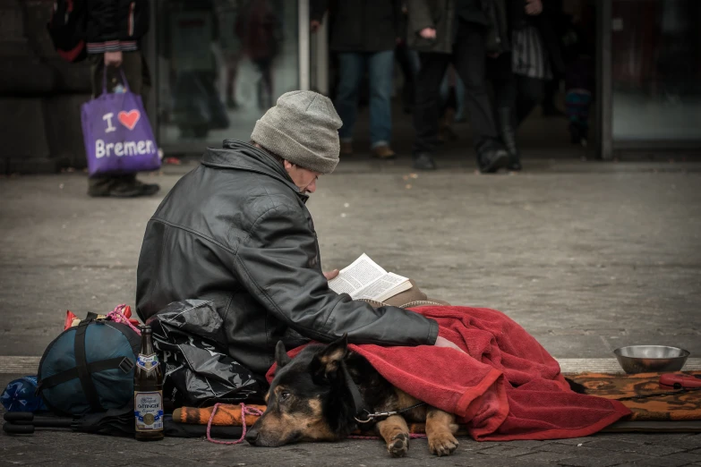 a person sitting on the ground with a dog under a blanket