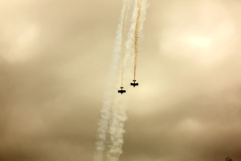 two airplanes flying together in the sky leaving trailing smoke behind them