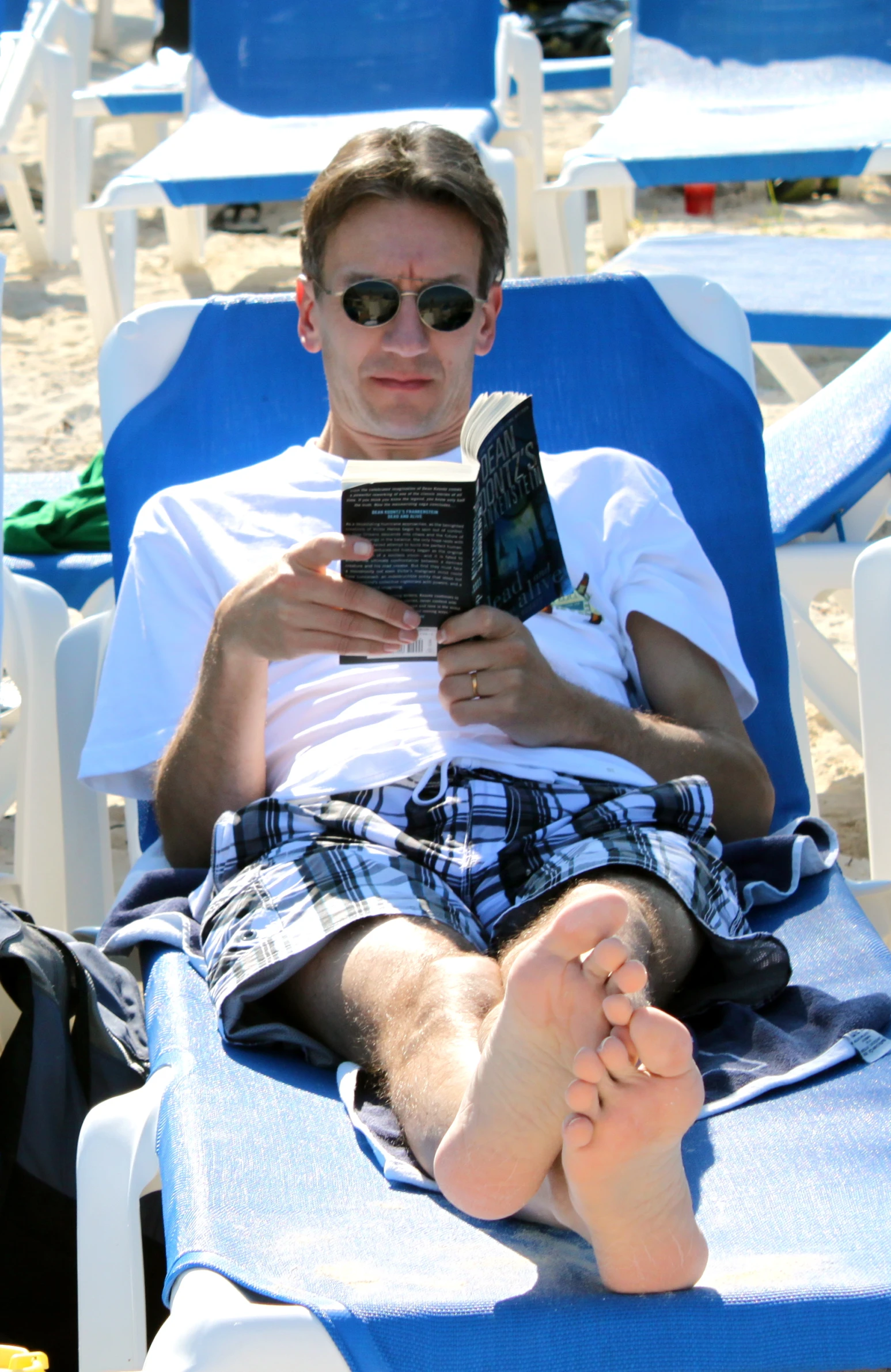 a man wearing sunglasses laying in lounge chairs while reading a book