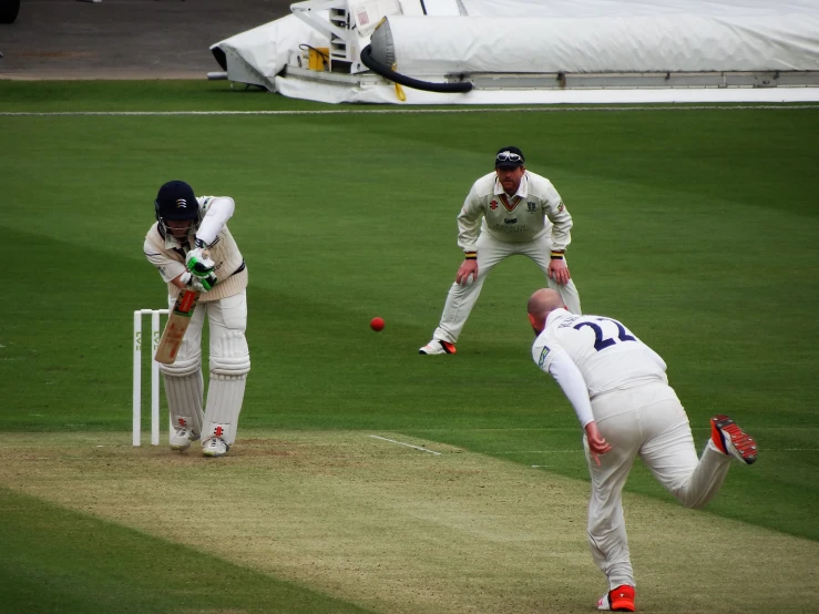three bowlers in white playing cricket in the middle of a pitch