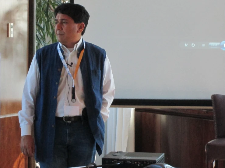 a man in vest and tie standing next to white screen