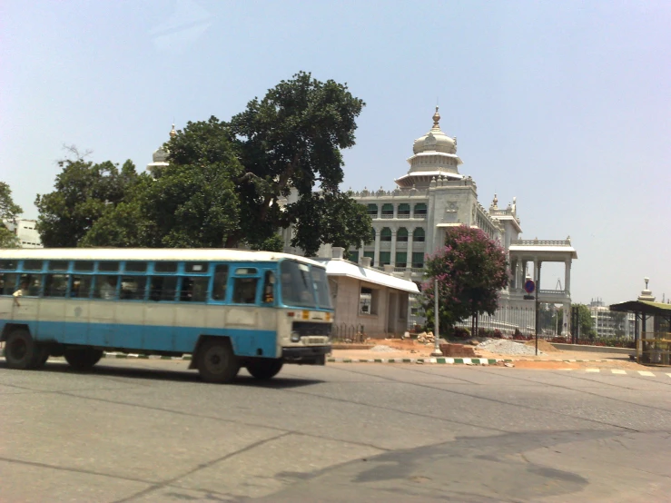 a blue and white bus is driving in front of a large building