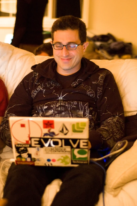 a man wearing glasses is sitting on the couch with his laptop