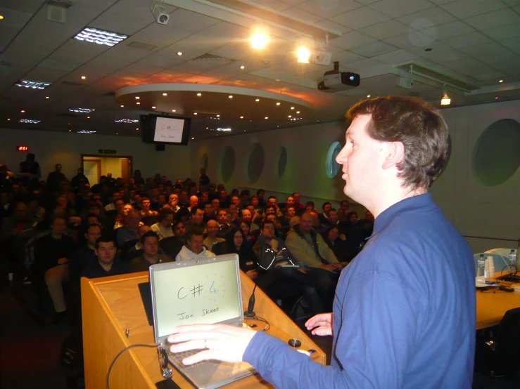 man speaking on a stage and people sitting in the auditorium