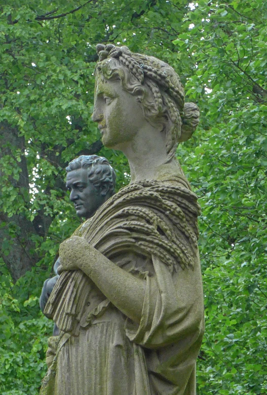 a statue with a cloak over it standing in front of trees