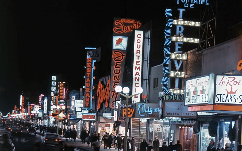 people walking on the sidewalk in front of some neon lights