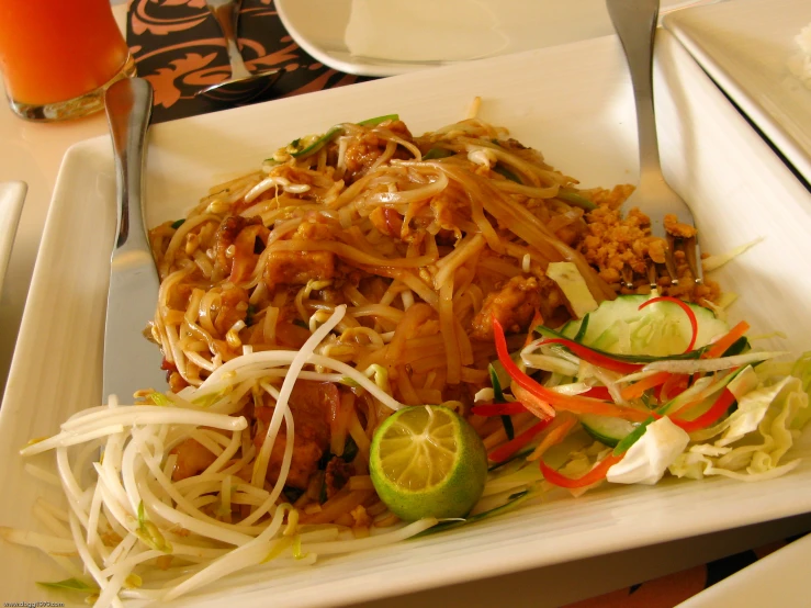 a white square plate of noodles and vegetables with sauce