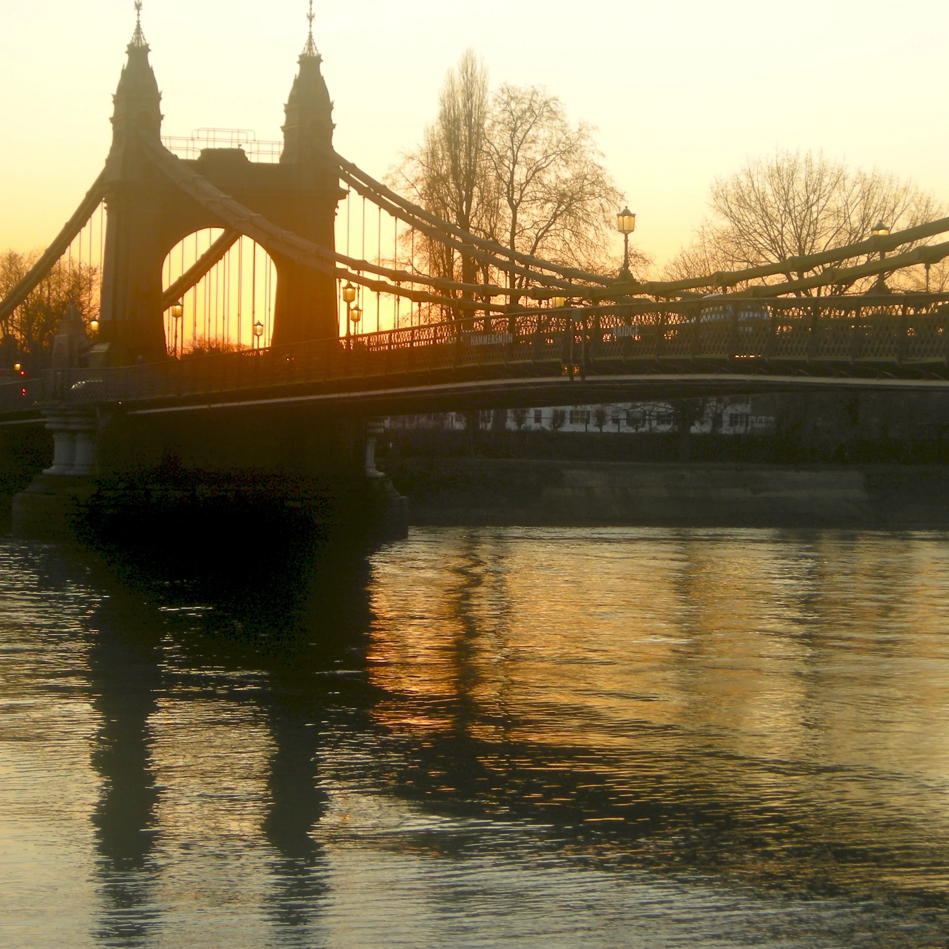 the sun is setting on a bridge over the water