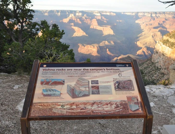 a sign near the side of a canyon that overlooks mountains and falls