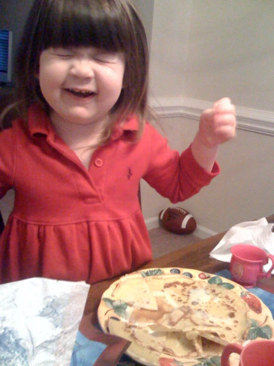 a little girl is laughing with a plate and napkin on a table