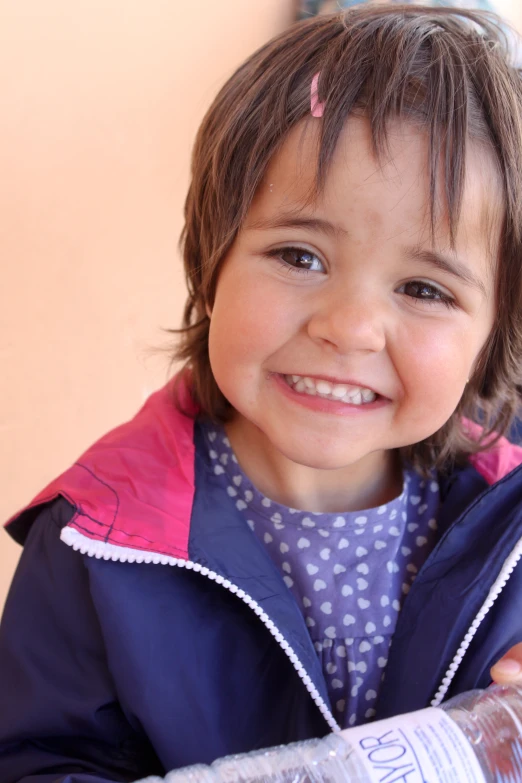 a little girl in purple jacket holding up a water bottle