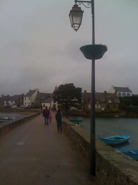 many people walking along a paved walkway near some boats