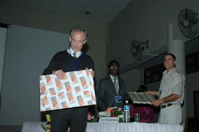 three people holding up wrapped presents and standing next to a table