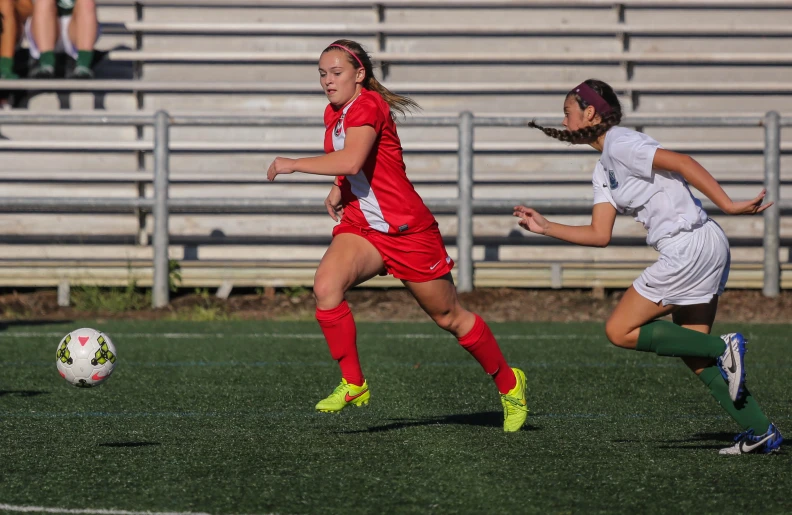 two women on opposite teams are chasing after the soccer ball