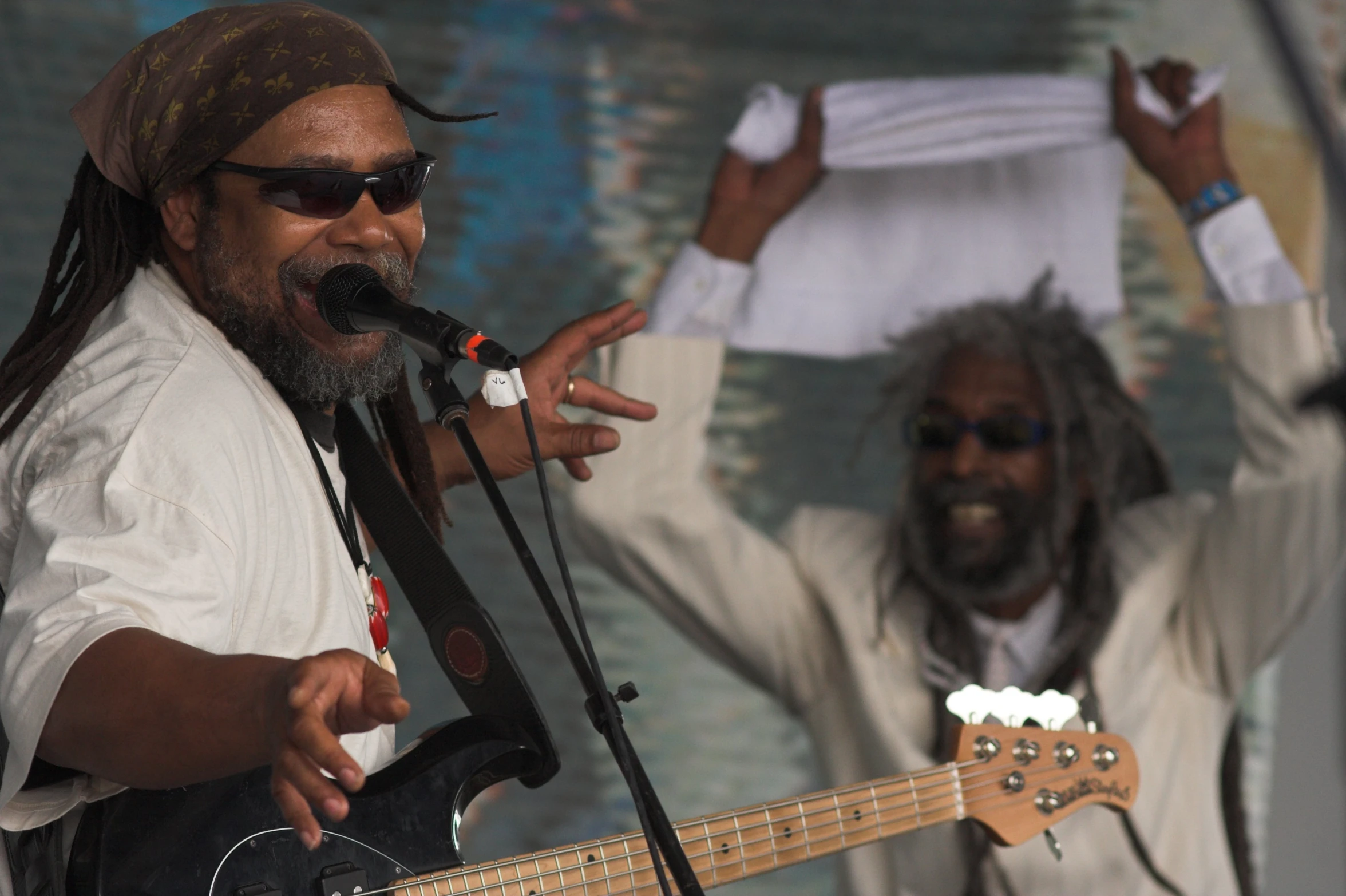 a bearded man in a white shirt singing with his bass guitar