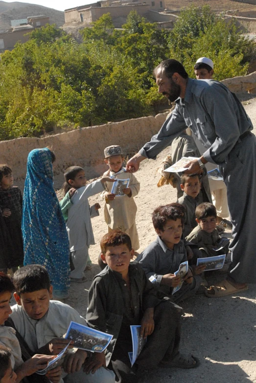 a man handing news to children in the middle of a dirt road