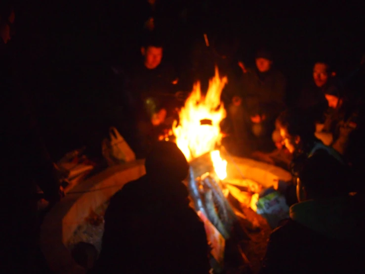 people sitting around a bonfire at night with their lights on