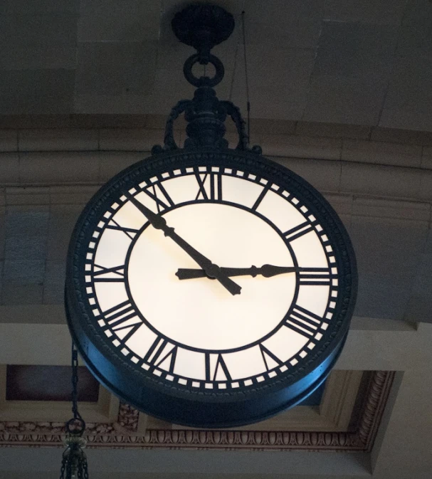 a large clock suspended from the ceiling with lighting underneath