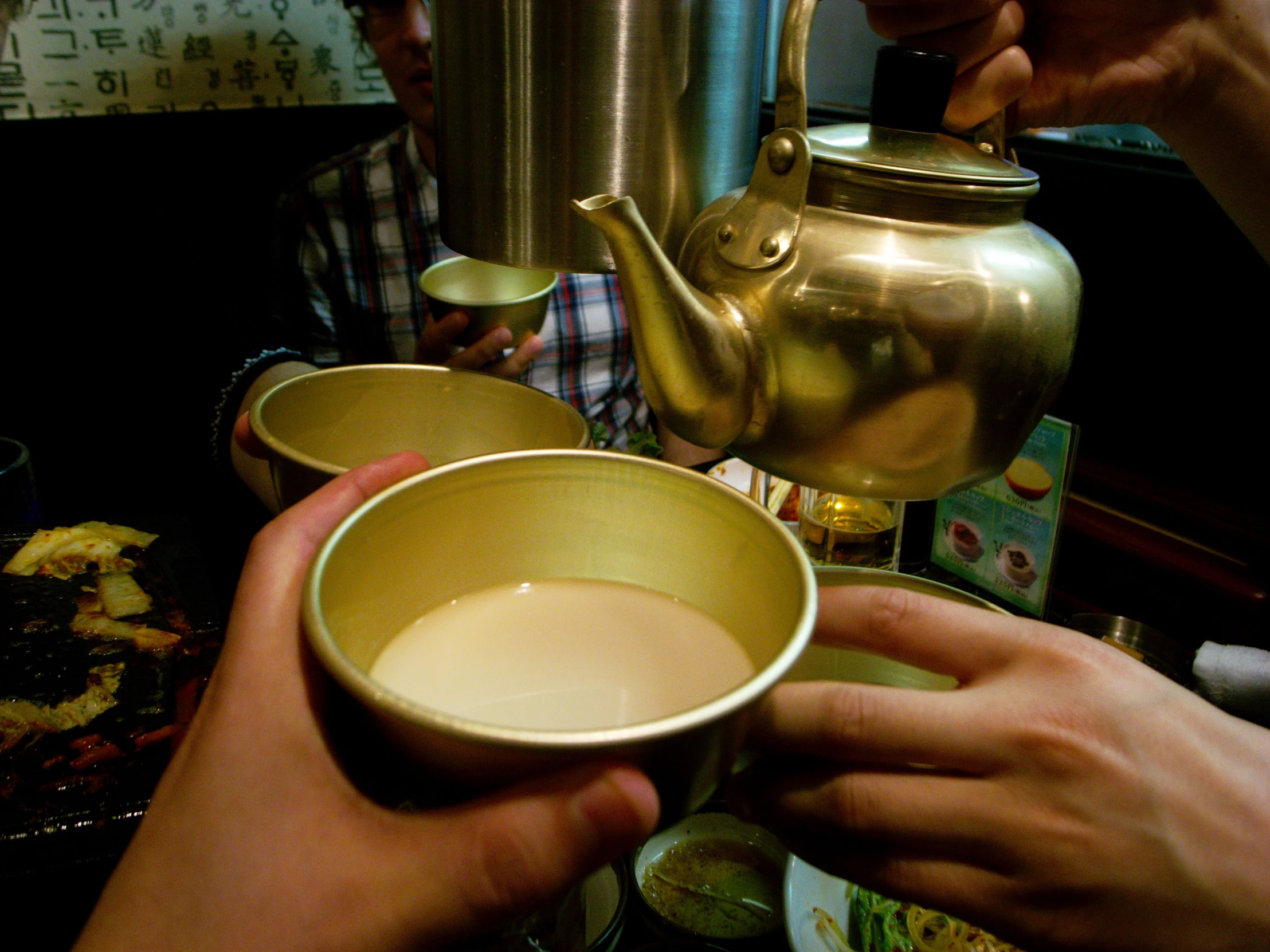 someone holding out their hand while making soing from the top of a metal tea pot