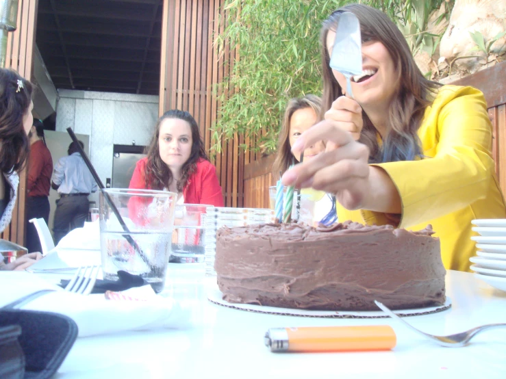 three girls stand at a table with a chocolate cake and an umbrella